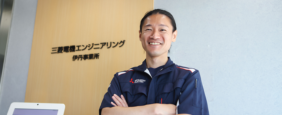 事業所のエントランス前で腕を組んで微笑む機械設計職の社員